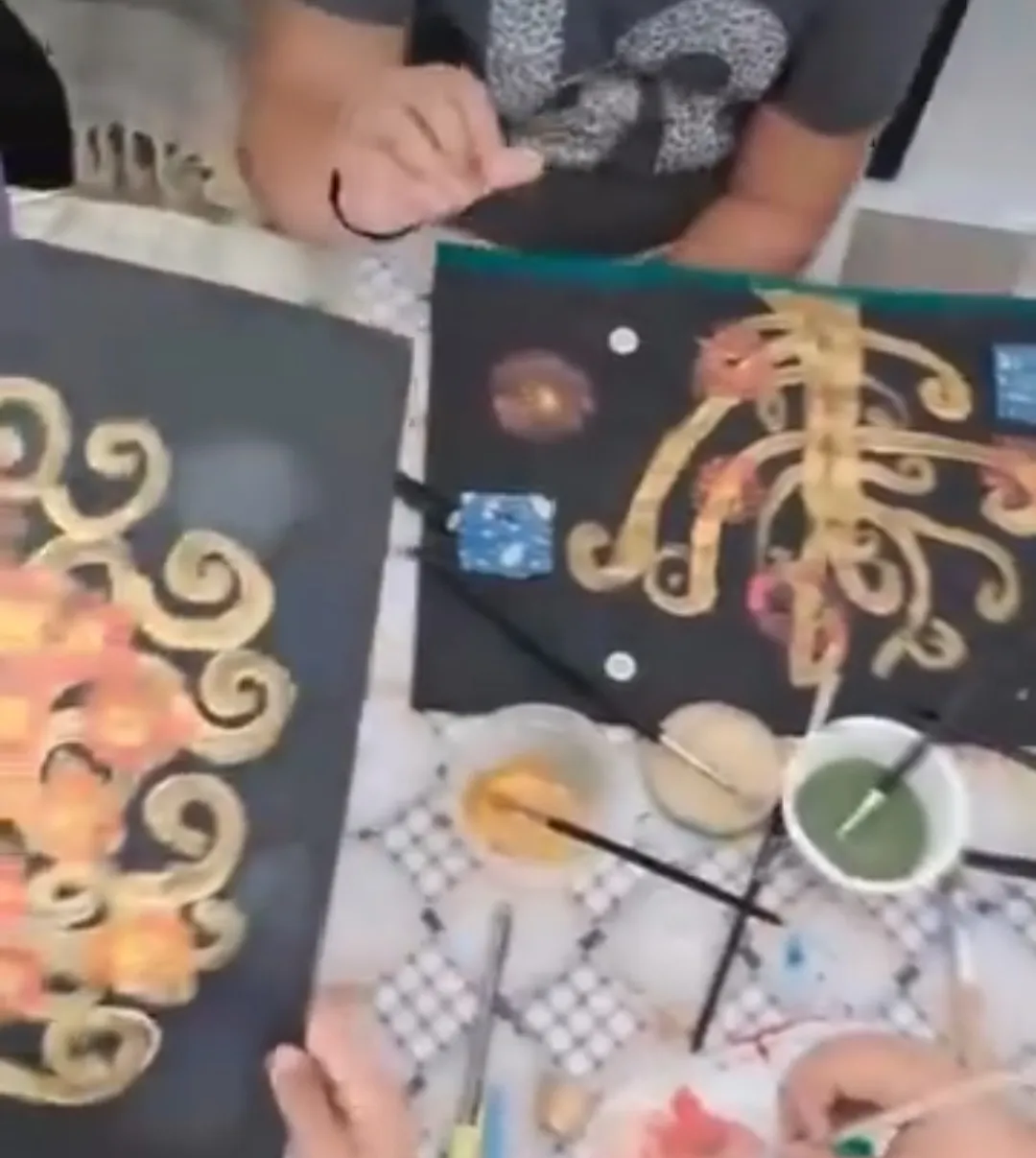 Dos lienzos negros con espirales doradas al estilo de Klimt sobre la mesa del taller