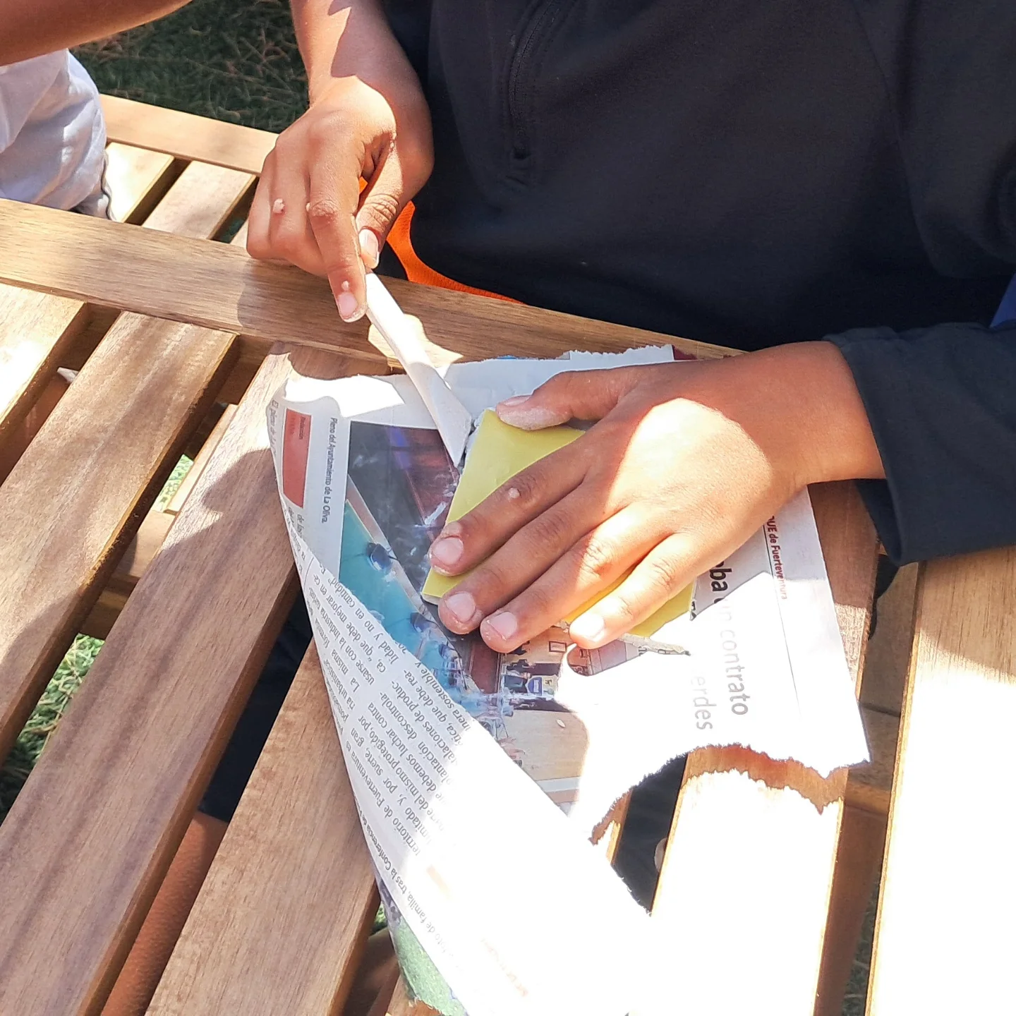 Manos recortando papel de periódico sobre la mesa del taller